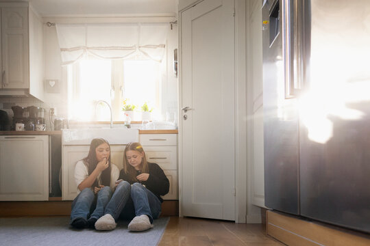 Multiracial female friends eating popcorn while sitting on kitchen floor at home