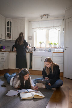 Multiracial female friends doing homework while sitting on kitchen floor in home