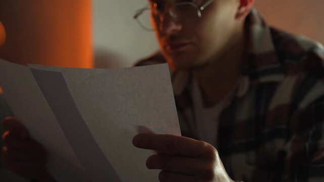 A student reads something on a white sheet of paper, preparing for a college exam.
He sits in a dark room in the evening, carefully studying the questions.