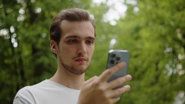 Young man using a smartphone in a green public park.