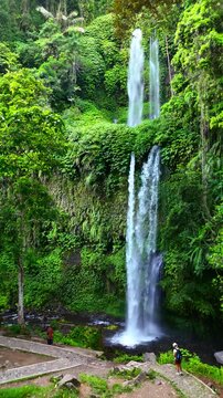 Aerial view of Sendang Gile Waterfall cascading through lush tropical jungle with people on a stone path in Kecamatan Bayan, Nusa Tenggara Barat, Indonesia.
