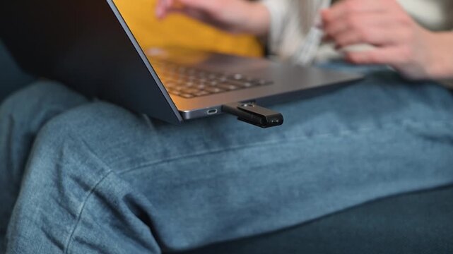 A person is using a USB drive to transfer data to a laptop while sitting on a couch