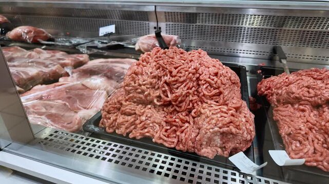 Raw minced meat on a tray inside a refrigerated display case in a grocery store's butcher section, ready for customers to purchase for cooking various meals like burgers or bolognese