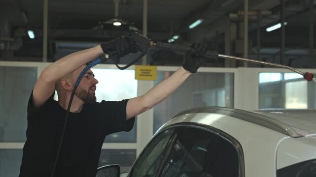 White Man Pressure Washing Car Roofline In Indoor Garage With High Wand And Focused Spray, Wearing Gloves