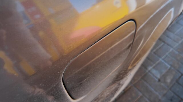 Close-up view of a hand unscrewing the fuel tank cap, screwing it back on after refueling the dirty car, and then closing the fuel filler door at a gas station before driving