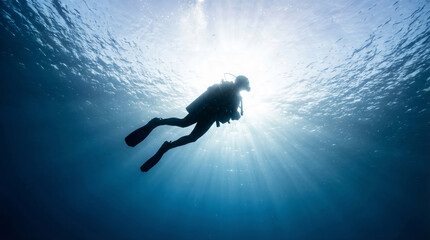 Fototapeta premium Silhouette of man diver swimming toward bright water surface with sun beams. Deep blue ocean background. Minimal underwater composition, exploration and freedom concept for adventure sport.