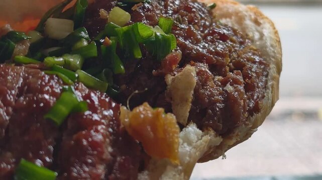 Extreme close up of Vietnamese street food Banh Mi Bo Nuong, showcasing juicy textures of grilled beef, authentic scallion oil, and crispy pork lard fatback