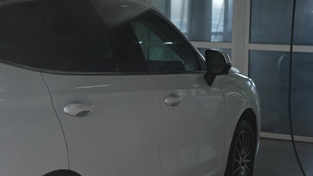 Man washing white SUV crossover with high-pressure washer at self-service car wash. Car cleaning and detailing concept