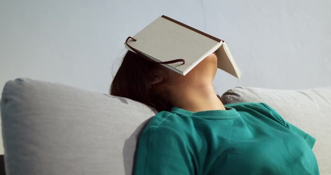A person relaxes at home humorously balancing a book their head showcasing a lighthearted moment.