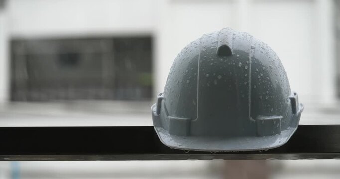 Raindrops on a white helmet against a backdrop of a construction site in the rain; rainy season and construction.