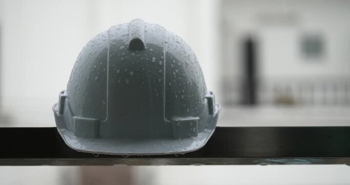 Raindrops on a white helmet against a backdrop of a construction site in the rain; rainy season and construction.