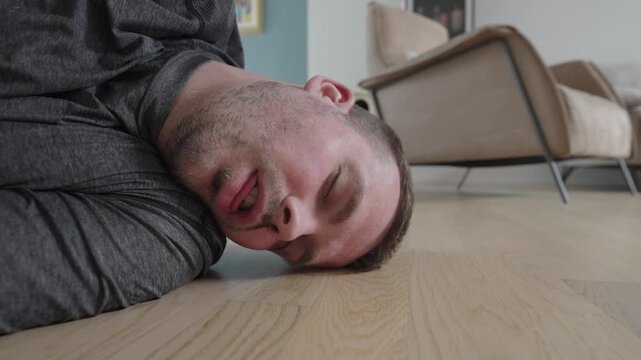 Close-up of an unconscious man being turned onto his side on the floor at home during a first aid emergency, showing recovery position, breathing check, medical assistance, care, and urgent health sup