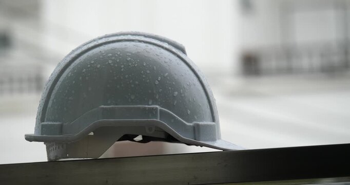 Raindrops on a white helmet against a backdrop of a construction site in the rain; rainy season and construction.