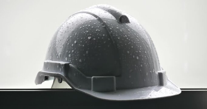 Raindrops on a white helmet against a backdrop of a construction site in the rain; rainy season and construction.