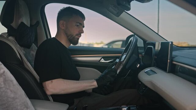 A man wearing gloves is cleaning the steering wheel of a car with a special brush and chemicals. Medium shot showing confident movements