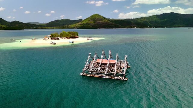 Aerial view of Gili Bedis island and a traditional fishing platform surrounded by turquoise waters and green hills in Sekotong, West Nusa Tenggara, Indonesia.