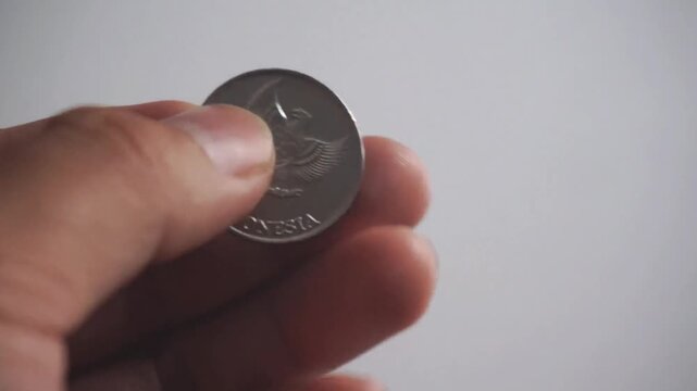 Close-up of a hand holding an Indonesian 200 rupiah silver coin.