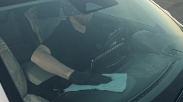 The man vigorously wipes the car interior with a soft cloth, removing dust from the dashboard with a microfiber cloth