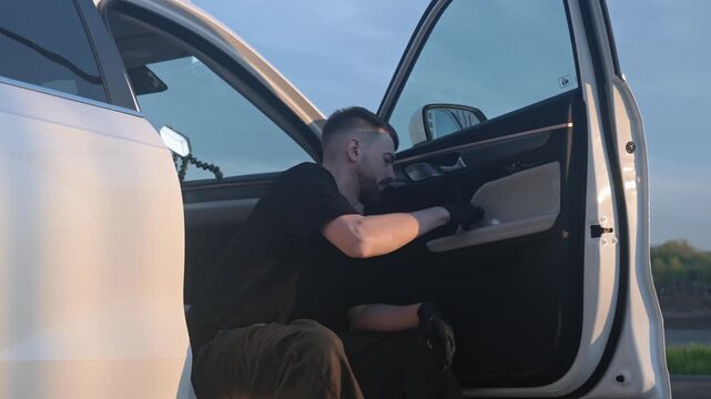 Caucasian Man carefully polishes the door frame and pocket of a car. Silhouettes against the backdrop of a sunset