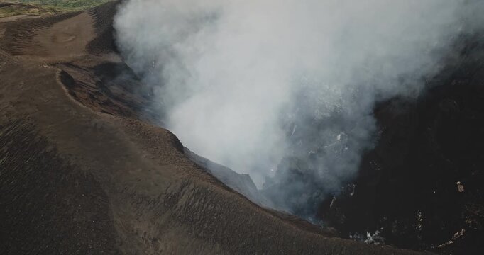 Mount Yasur volcano crater actively emitting large plume of white smoke and ash into the sky, revealing dynamic geological power on Tanna Island, Vanuatu. Dramatic landscape. Aerial drone flight shot