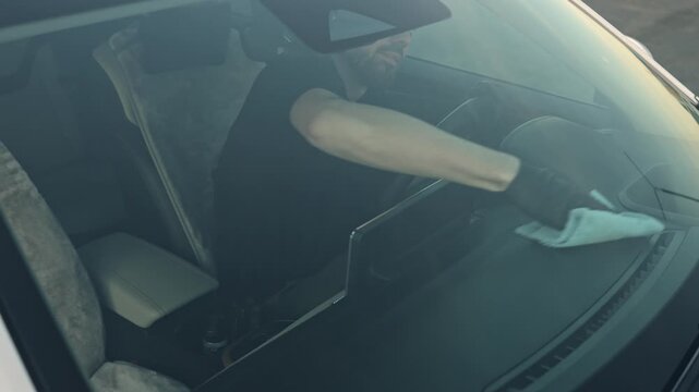 man wipes the dashboard to remove streaks. Smooth hand movements, a microfiber cloth, and a late evening