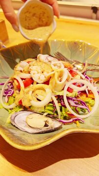Vertical video. Fresh Seafood Salad With Squid Rings Shrimp Mussel and Vegetables While Creamy Dressing Is Poured Above Bowl, Gourmet Healthy Eating