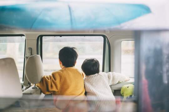 Two children looking outside from car window on rainy day
