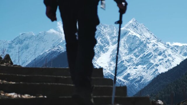 Cinematic shot of a trekker climbing stone steps with the majestic snow-capped Manaslu peaks dominating the background.