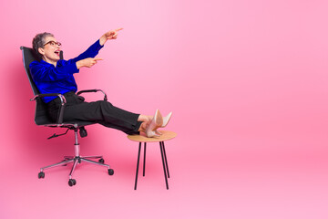 Fototapeta premium Confident senior businesswoman relaxes in pink studio pointing with smile
