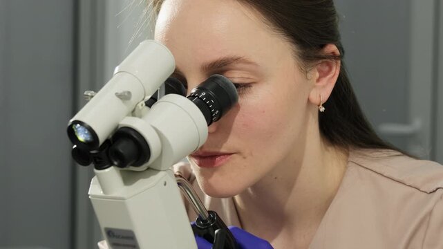Microscope frames gynecologist during cervical sample inspection in clinic. Doctor observes specimen closely maintaining steady visual analysis