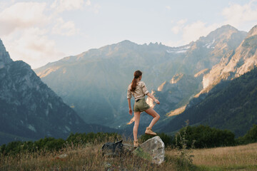 Fototapeta premium A woman hiking on a rocky outcrop beside a valley in the mountains, exploring nature and enjoying outdoor freedom, sun shining over alpine terrain.
