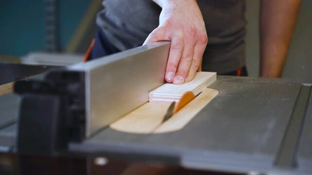 Circular table saw cutting wood in carpenter workshop close up. A running blade on a bench saw sawing trough the wooden log in the middle of a working space, close up footage. 