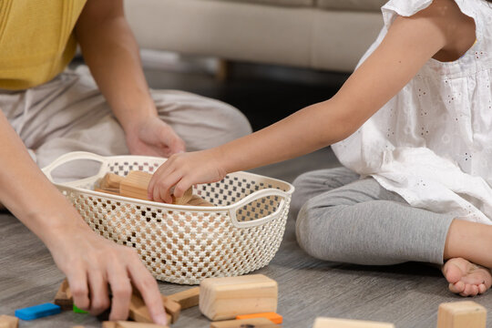 Asian mother teaching daughter good habit through cleaning toys, child placing blocks into basket with guidance, child development, supports discipline and organization skill, early childhood activity