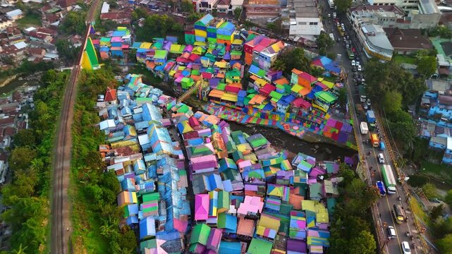 Aerial view of the vibrant colorful houses of Kampung Warna Warni Jodipan along the riverbank and railway Kecamatan Blimbing, Jawa Timur, Indonesia.