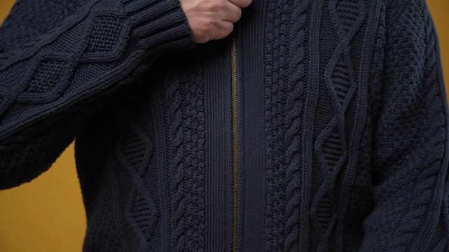 Close-up of a person zipping up a dark blue cable knit cardigan sweater.