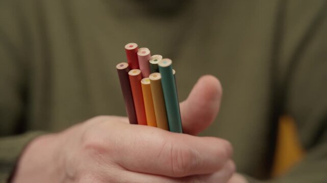 Close-up of a person holding a bunch of unsharpened colored pencils in hand.