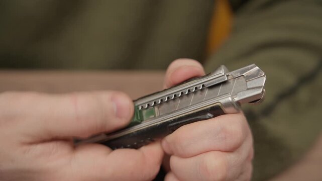 Close-up of a worker holding a retractable utility knife with a sharp metal blade