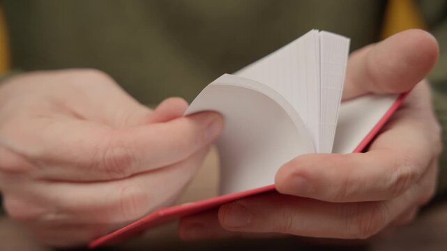 Close-up of hands quickly flipping through the blank white pages of a small red book.