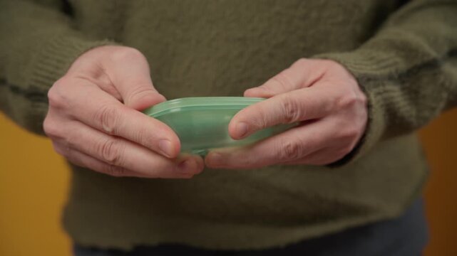 male hands opening a small green semi-transparent plastic container.