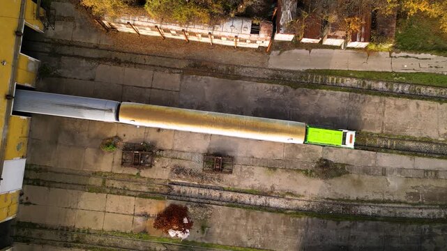 Aerial view of a railway maintenance depot with several passenger train carriages parked on parallel tracks beside a large workshop building, showing rail infrastructure, rolling stock and servicing f