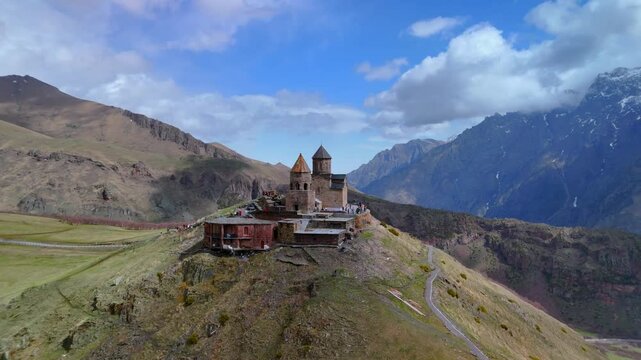 Aerial view of Gergeti Trinity Church standing on a mountain ridge with people walking around the stone walls in Mtskheta-Mtianeti, Georgia.