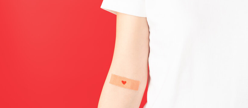 Blood donation. Human hands with plaster heart on arm against red background. Hematologic disorders such as anemia, sickle cell disease, hemophilia, leukemia and ITP.