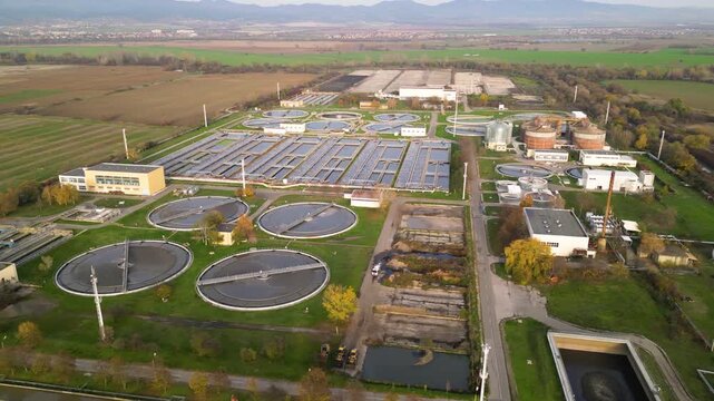 Aerial view of a wastewater treatment plant with multiple large circular clarifier tanks, sedimentation basins, channels and filtration structures arranged in a geometric industrial water-processing c