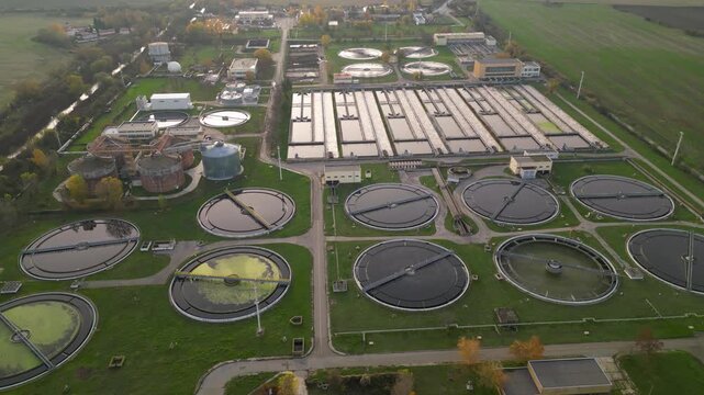 Top-down aerial image of an extensive municipal water treatment complex with multiple round clarifier tanks, long filtration channels, administrative buildings, and access roads bordered by farmland a
