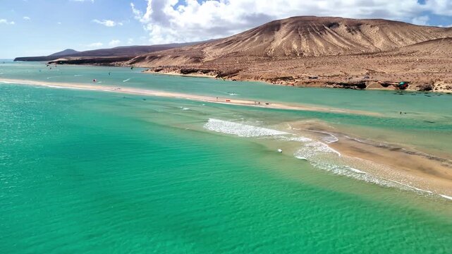 Aerial view of Playa del Matorral sandbar with turquoise ocean water and volcanic hills under a sunny sky, Canary Islands, Spain.