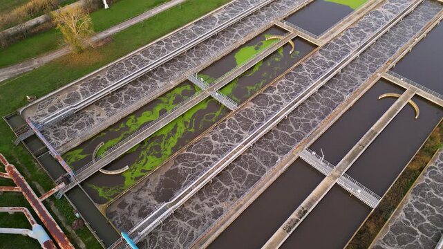 Top-down aerial image of an extensive municipal water treatment complex with multiple round clarifier tanks, long filtration channels, administrative buildings, and access roads bordered by farmland a