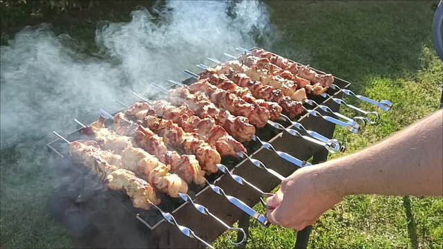 Man cooking traditional shashlik meat skewers on charcoal grill outdoors. BBQ picnic concept. Sausages on the grill.