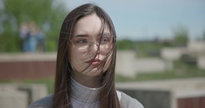 Close-up portrait of a young white female student wearing glasses with long dark hair in a park
