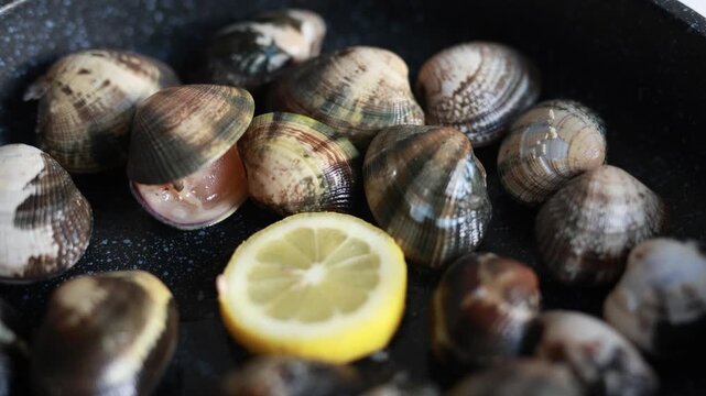 Close-up of cooking fresh clams in a pan with lemon, garlic and herbs