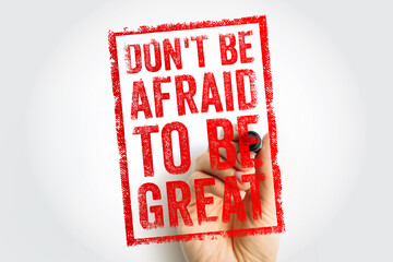 Naklejka premium DONT BE AFRAID TO BE GREAT motivational quote written on transparent surface. Hand holds marker near stamp style text encouraging confidence, success, and personal growth.